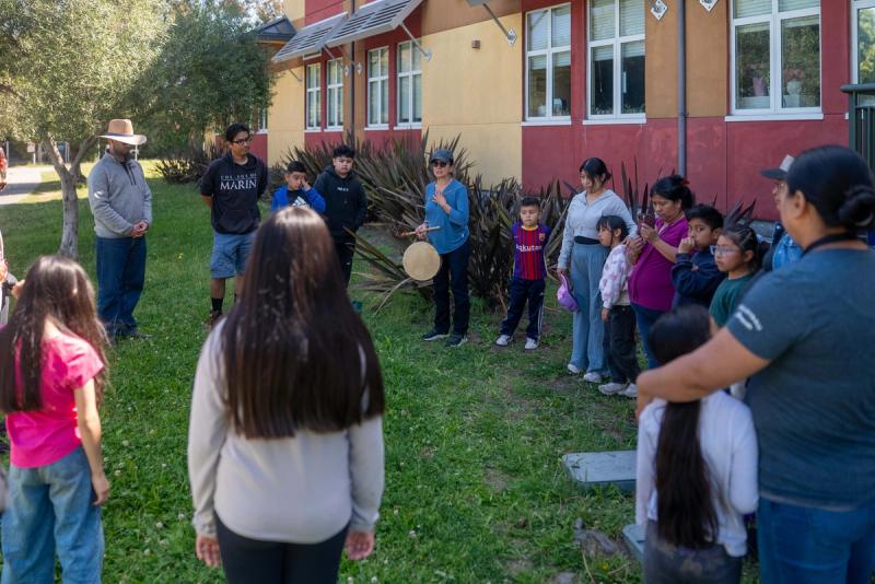 Children and adults gathered in a circle on the grass with drums