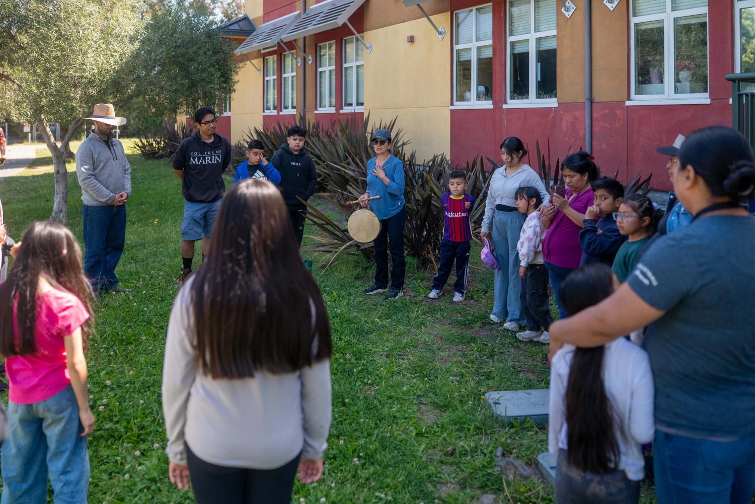 Children and adults gathered in a circle on the grass with drums