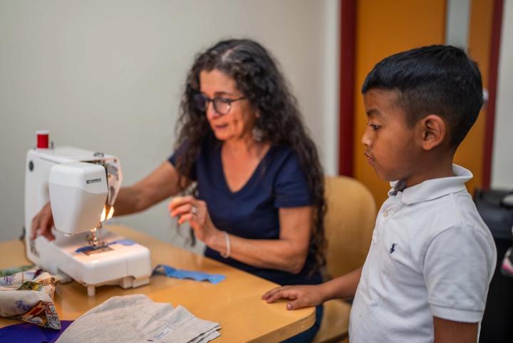 An adult guiding a young person at a sewing machine