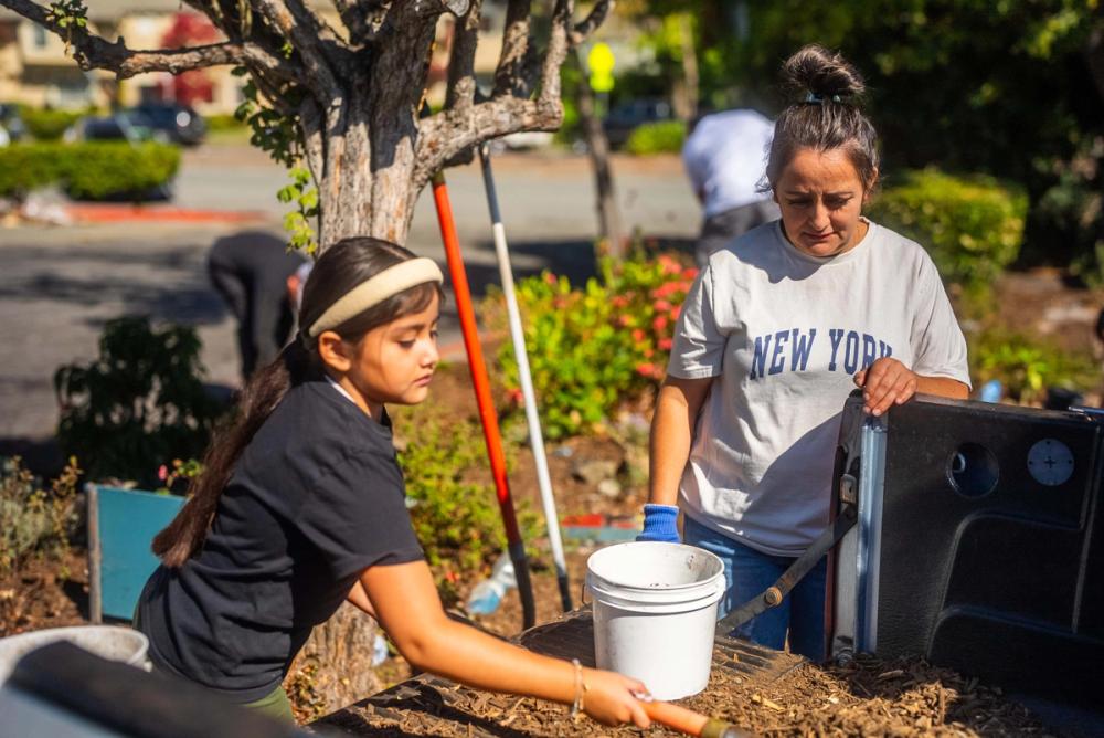 Young people and an adult working with buckets beside a garden at a previous Minga