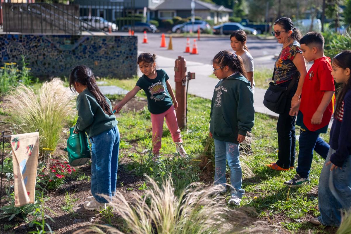 Students gathered with an instructor as a classmate waters flowers at Bahía Vista Elementary