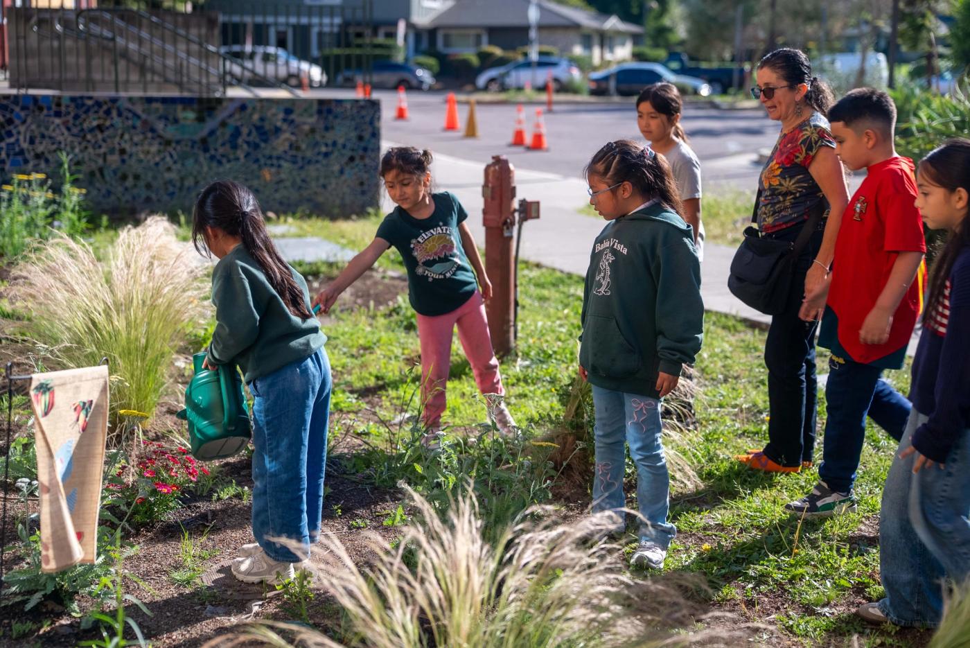 Students gathered with an instructor as a classmate waters flowers at Bahía Vista Elementary