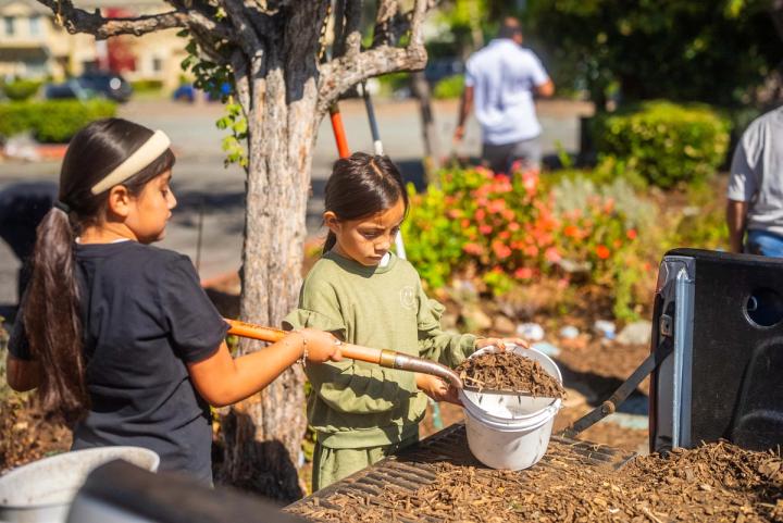 Students and an adult working with buckets beside the community garden and pickup truck