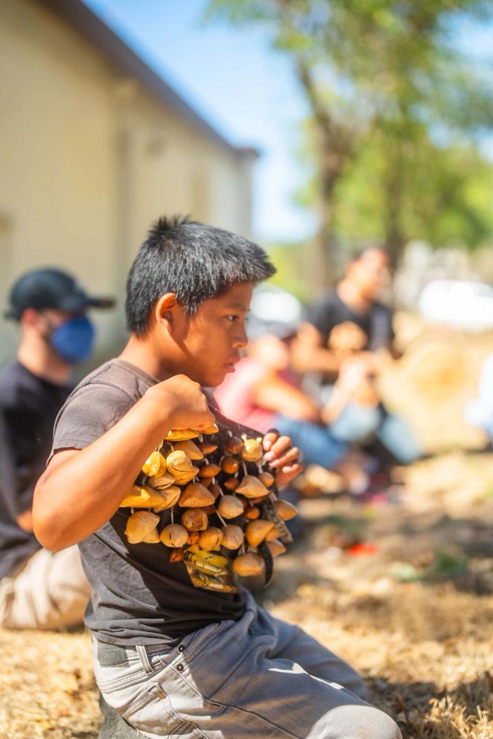 A young participant holding a cluster of rattles while seated in the outdoor circle