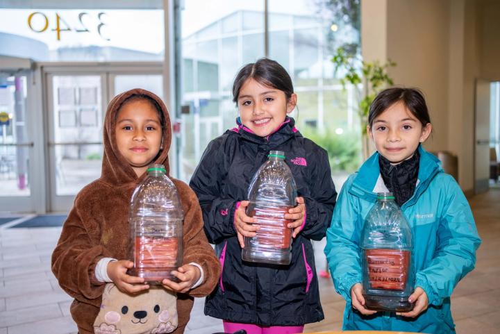 Three children holding their recycled-bottle planting projects
