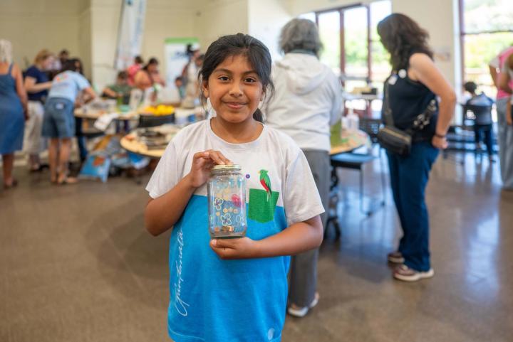 A smiling child holding a handmade project at a community event