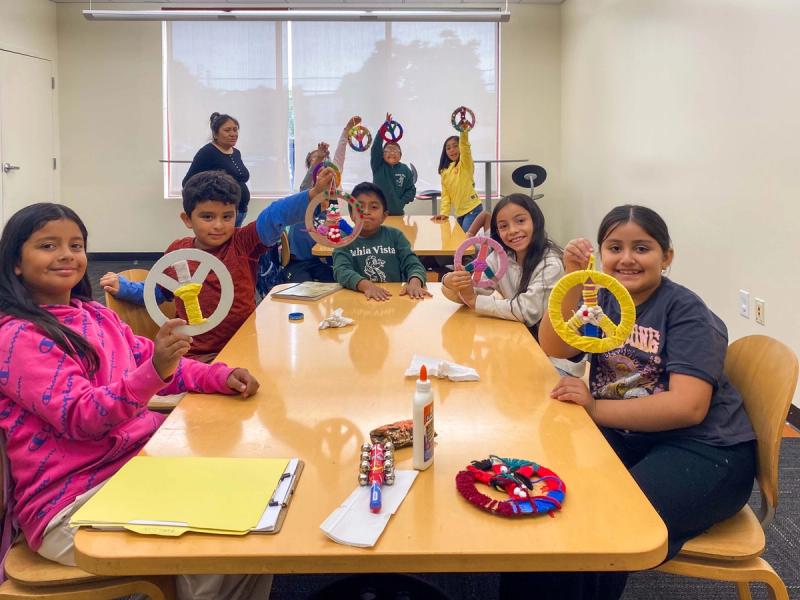 Students gathered around a classroom table holding colorful handmade paper shapes