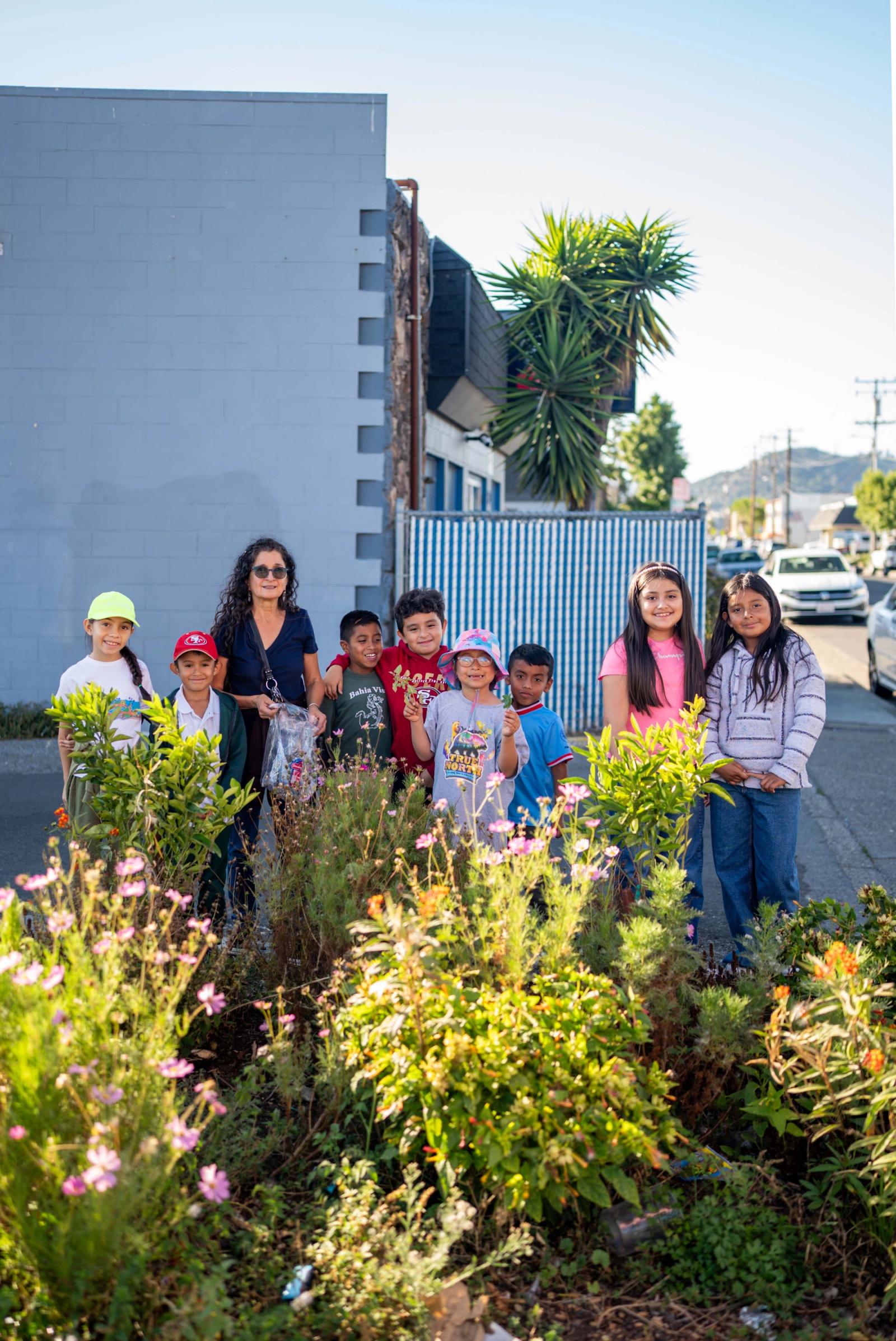 Children and an adult smiling among flowers in their neighborhood garden
