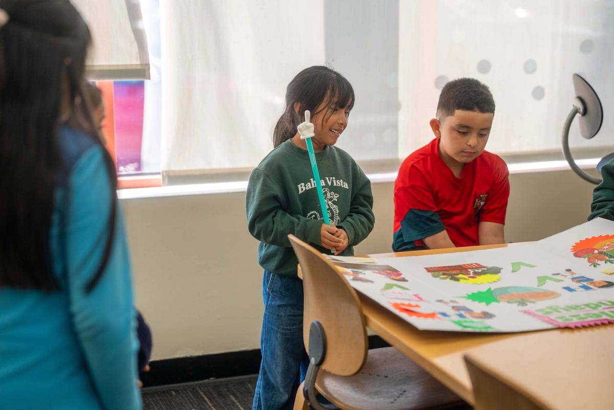 Two students standing beside a colorful tabletop display while classmates sit nearby