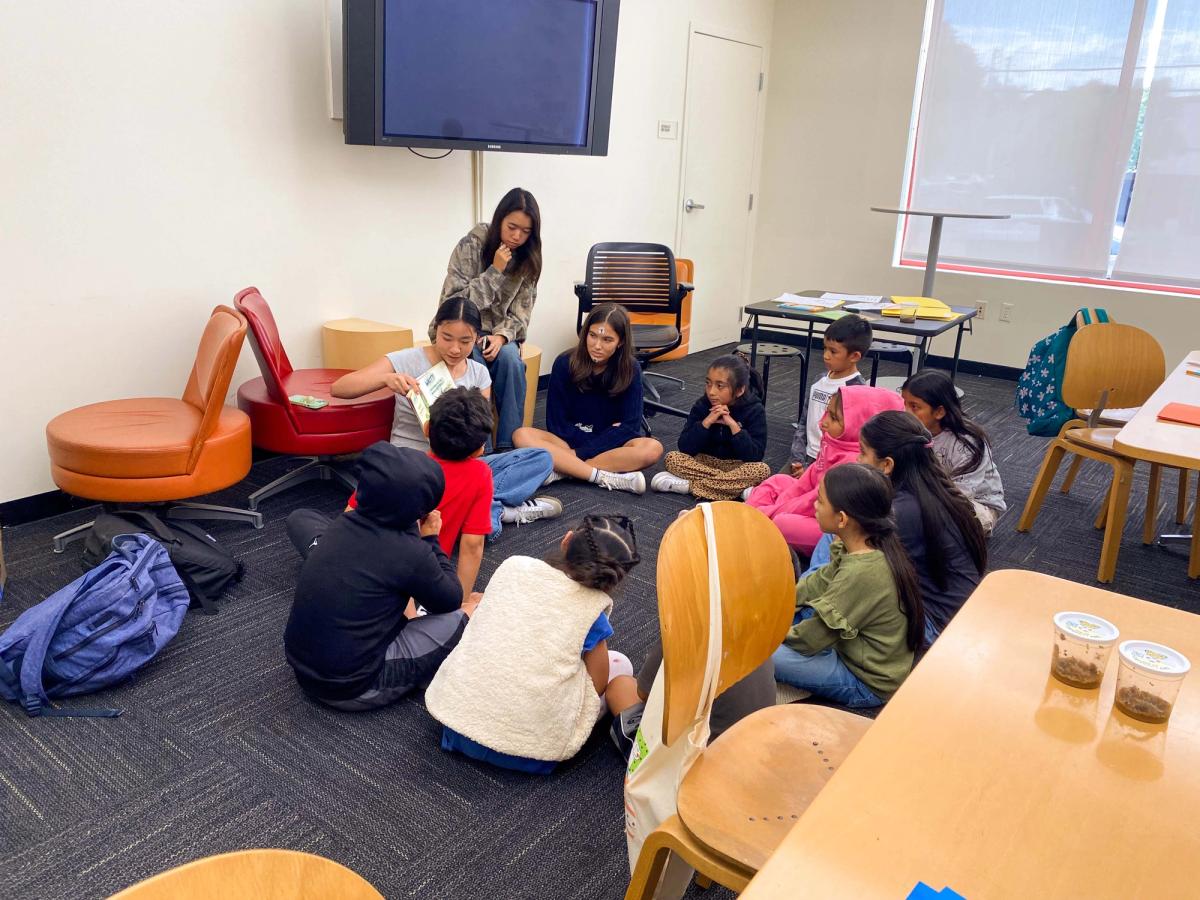 Students seated together on a classroom rug with an adult leading a group activity