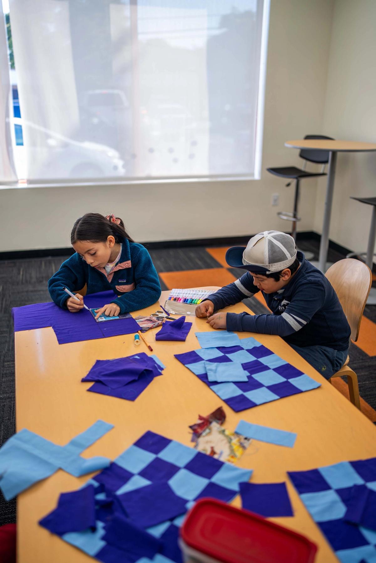Students working with blue fabric squares spread across a classroom table