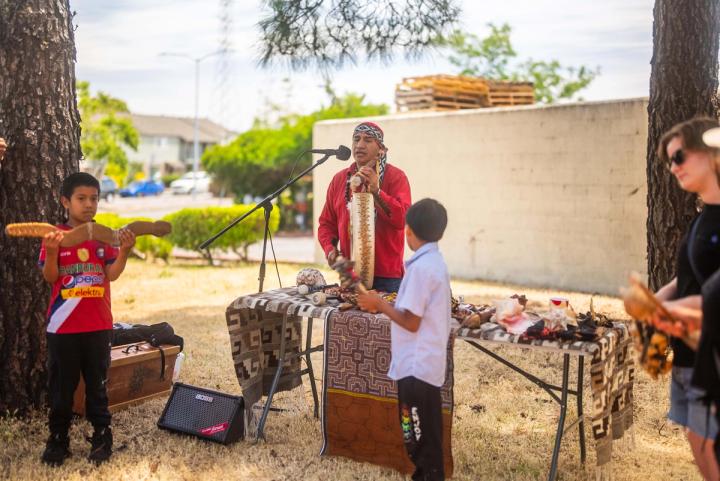 An adult and young people with drums during an outdoor gathering