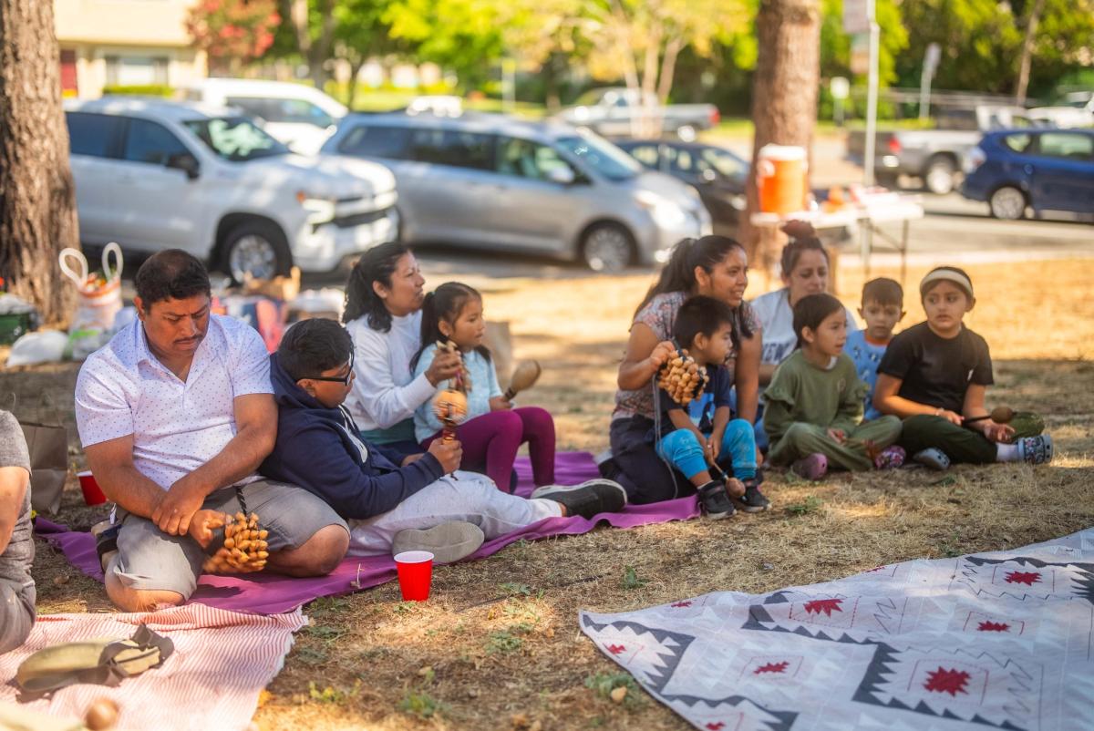 Students and adults sitting together in an outdoor circle beneath the trees