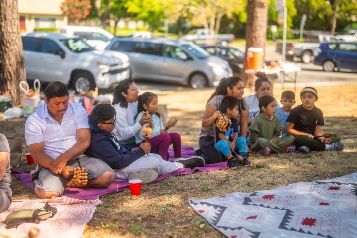 Students and adults sitting together in an outdoor circle beneath the trees