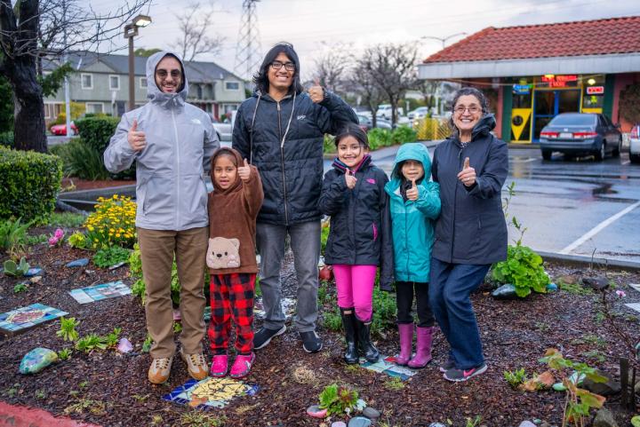 A group of children and adults standing together in a neighborhood garden on an overcast day