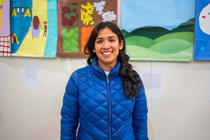 A smiling person in a blue jacket standing in front of colorful artwork