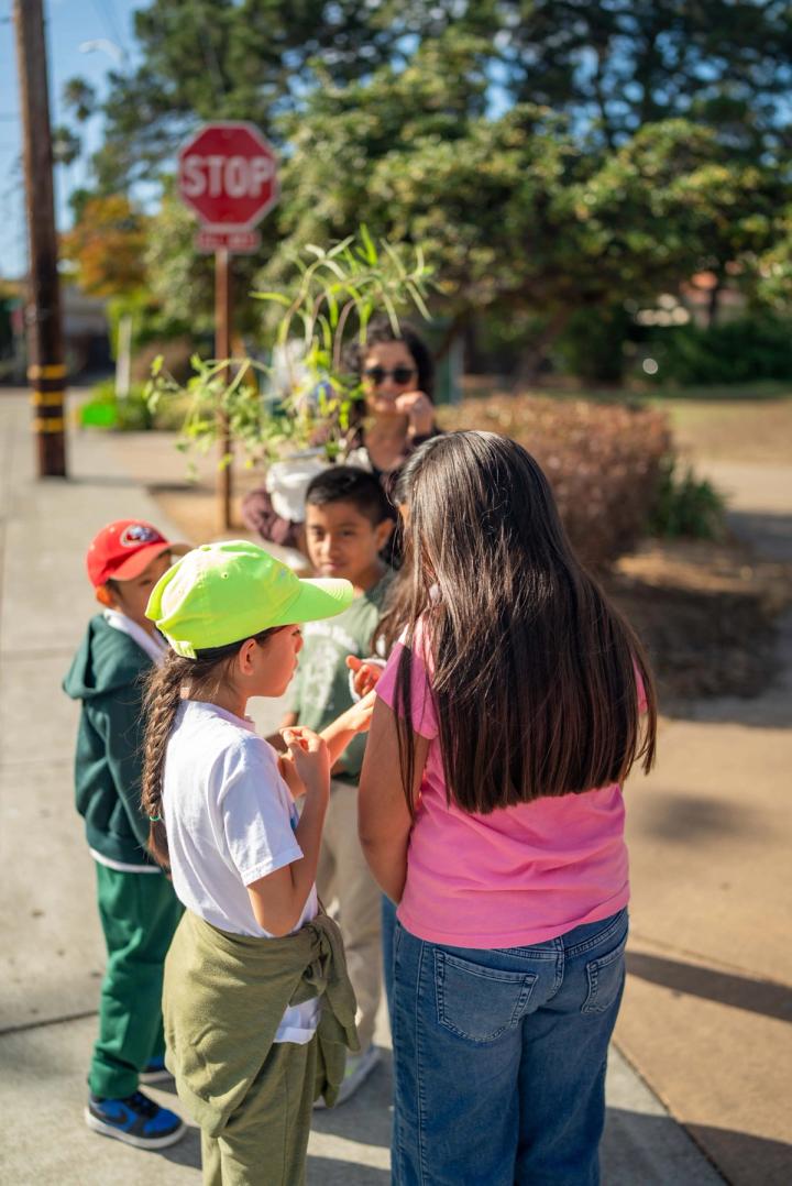 Young people gathered with an adult near plants at a neighborhood street corner