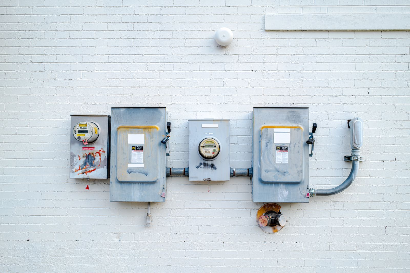 Plusieurs compteurs électriques fixés sur un mur blanc, avec des câbles et des boîtiers de répartition