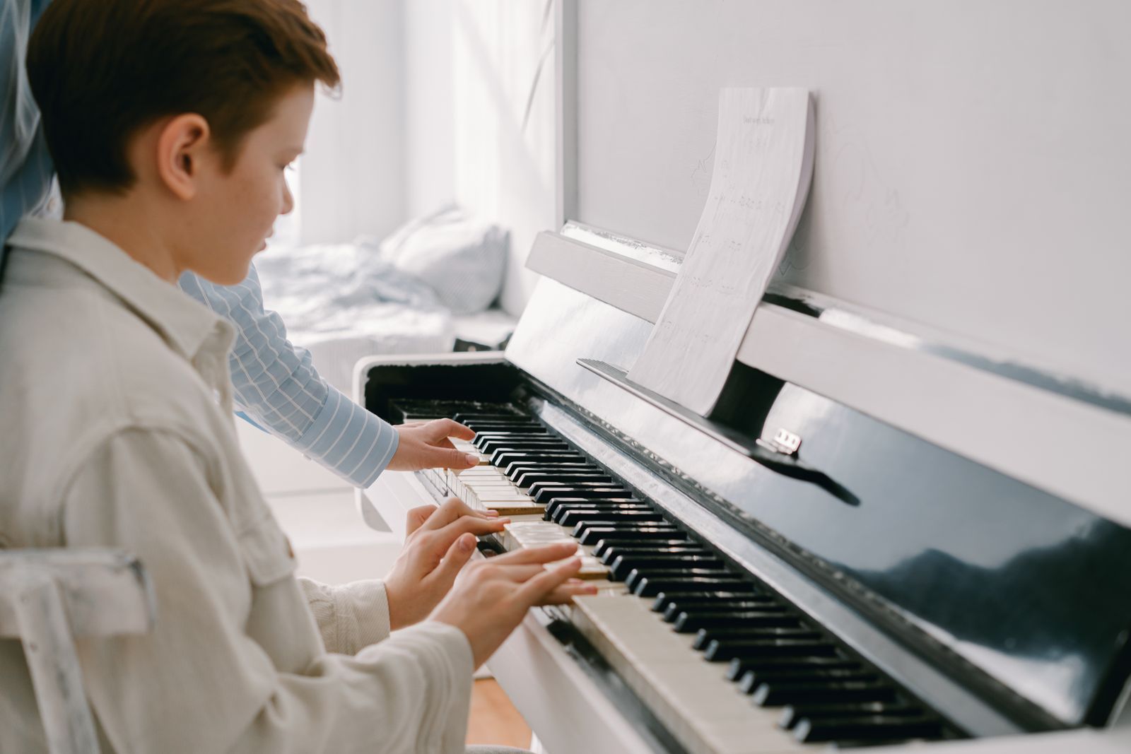 Jeune garçon jouant sur un piano numérique meuble blanc, partition ouverte devant lui