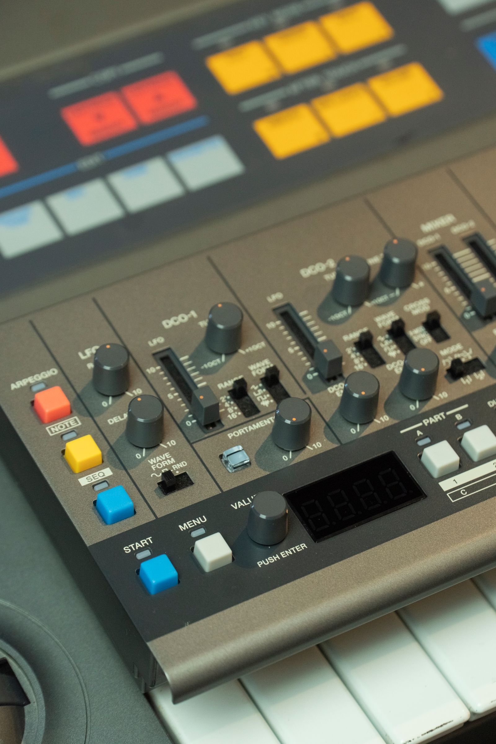 Gros plan sur des potentiomètres et des réglages d'un synthétiseur, avec touches blanches et noires en bas de l'image