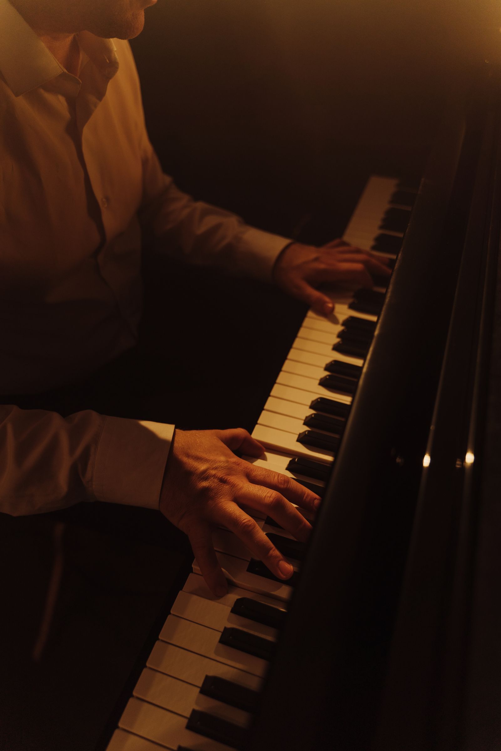 Mains posées sur les touches d'un piano numérique haut de gamme dans une lumière chaude et feutrée