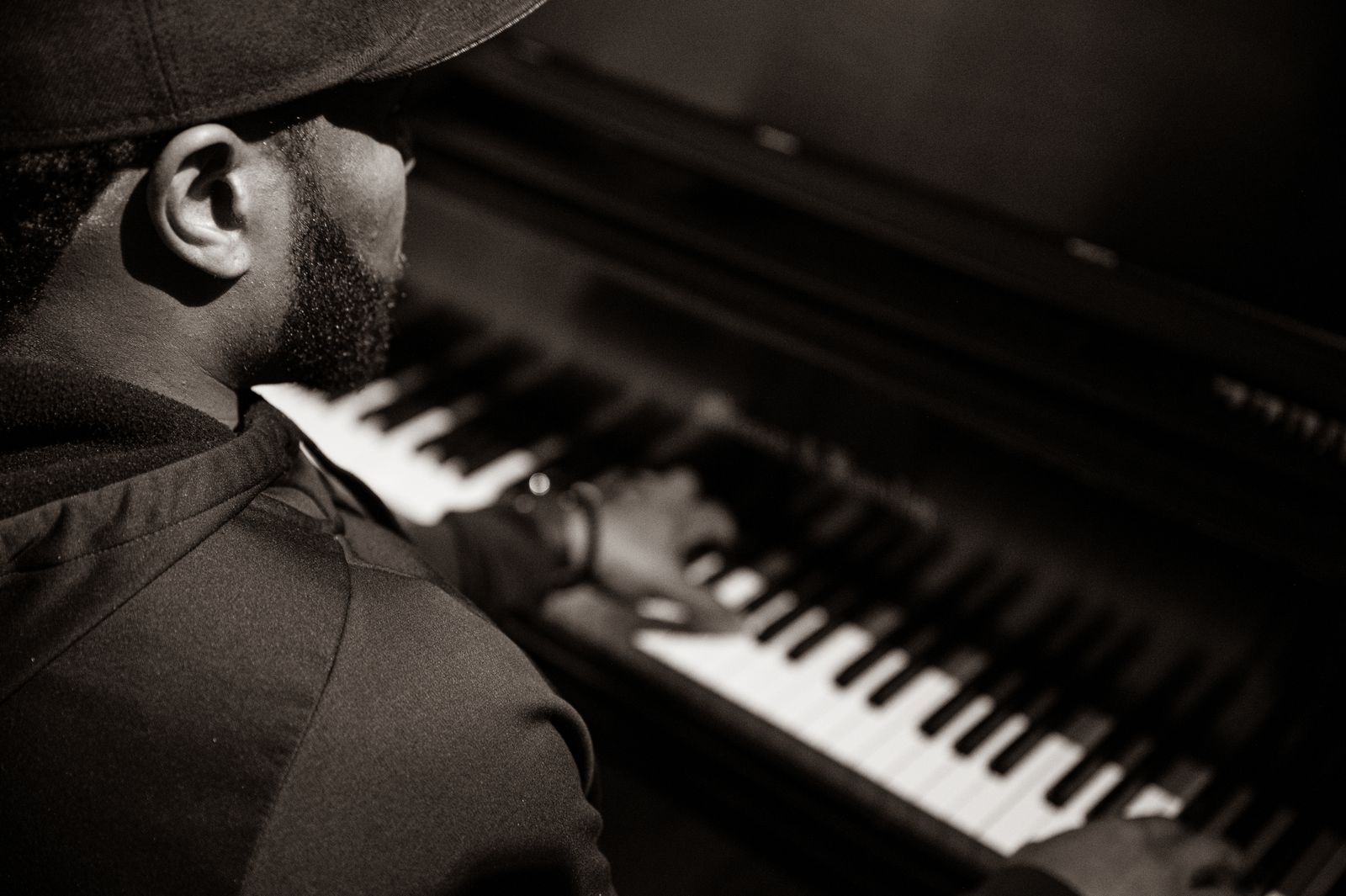 Pianiste jouant dans une lumière sombre, avec des mains posées sur un piano à queue et une silhouette en arrière-plan