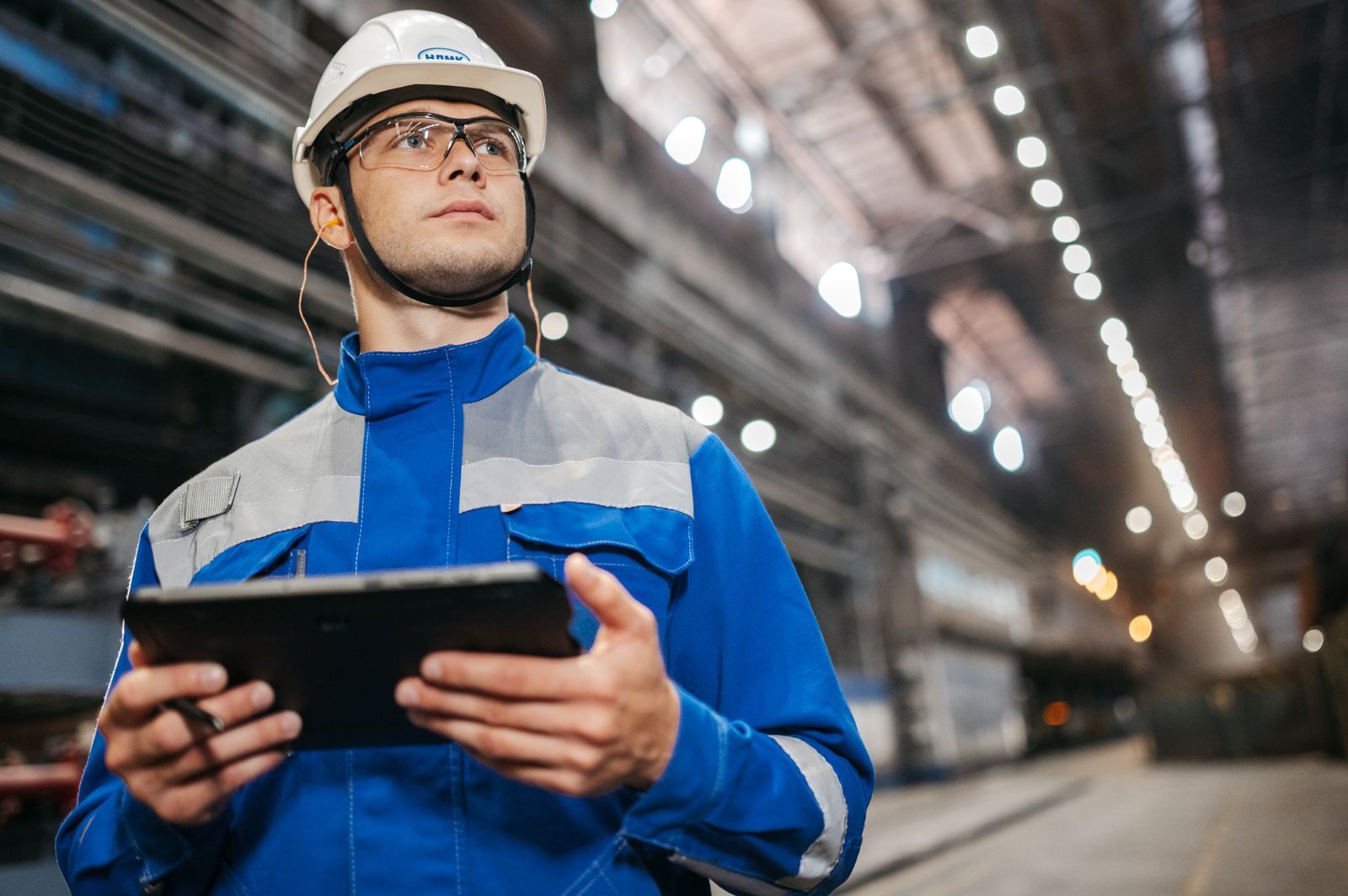 Technicien en tenue de travail tenant une tablette dans un environnement industriel