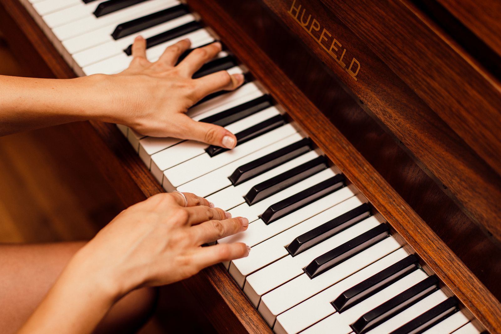 Deux mains posées sur les touches d'un piano en bois