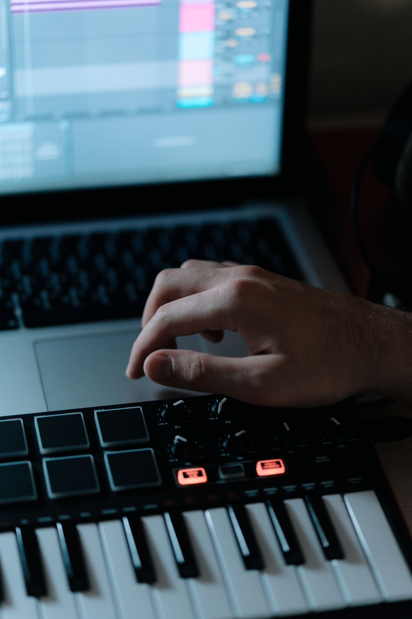Mains posées sur un clavier maître alors que l'écran d'un ordinateur affiche une station de production musicale