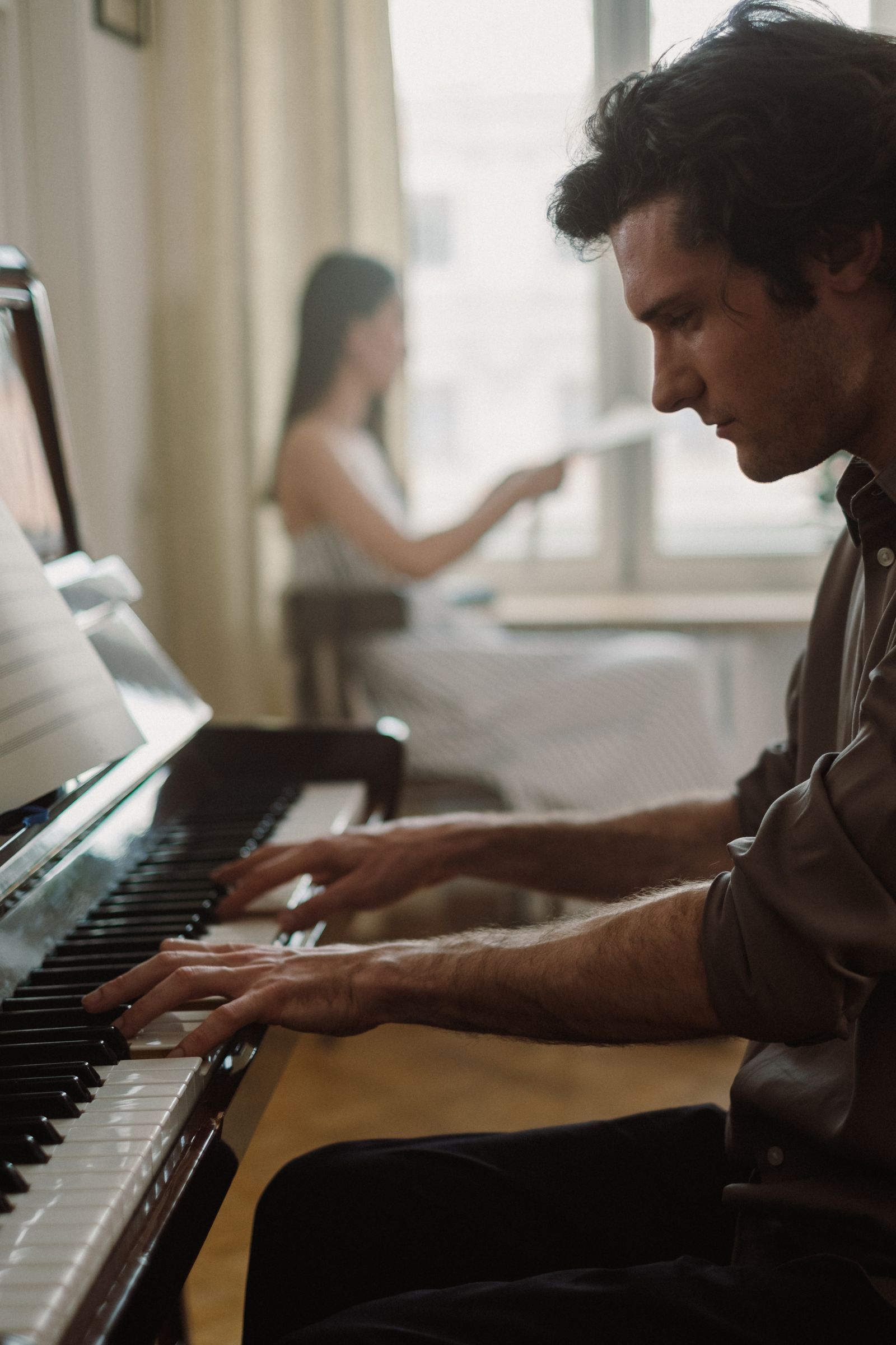 Homme jouant du piano à queue dans un salon lumineux, avec une personne en arrière-plan