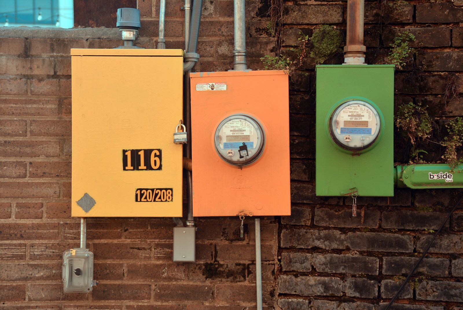 Plusieurs boîtiers de compteurs électriques colorés, fixés sur un mur de brique