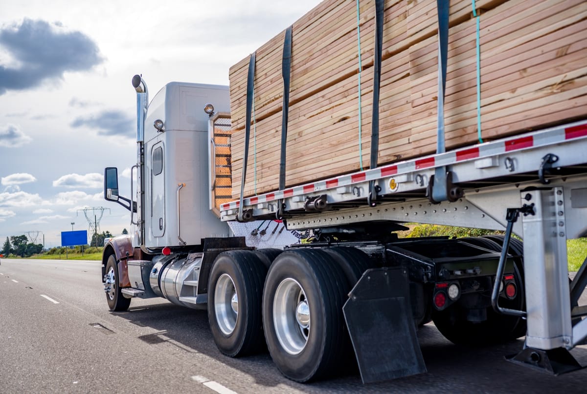 A flatbed truck carrying banded lumber on the highway