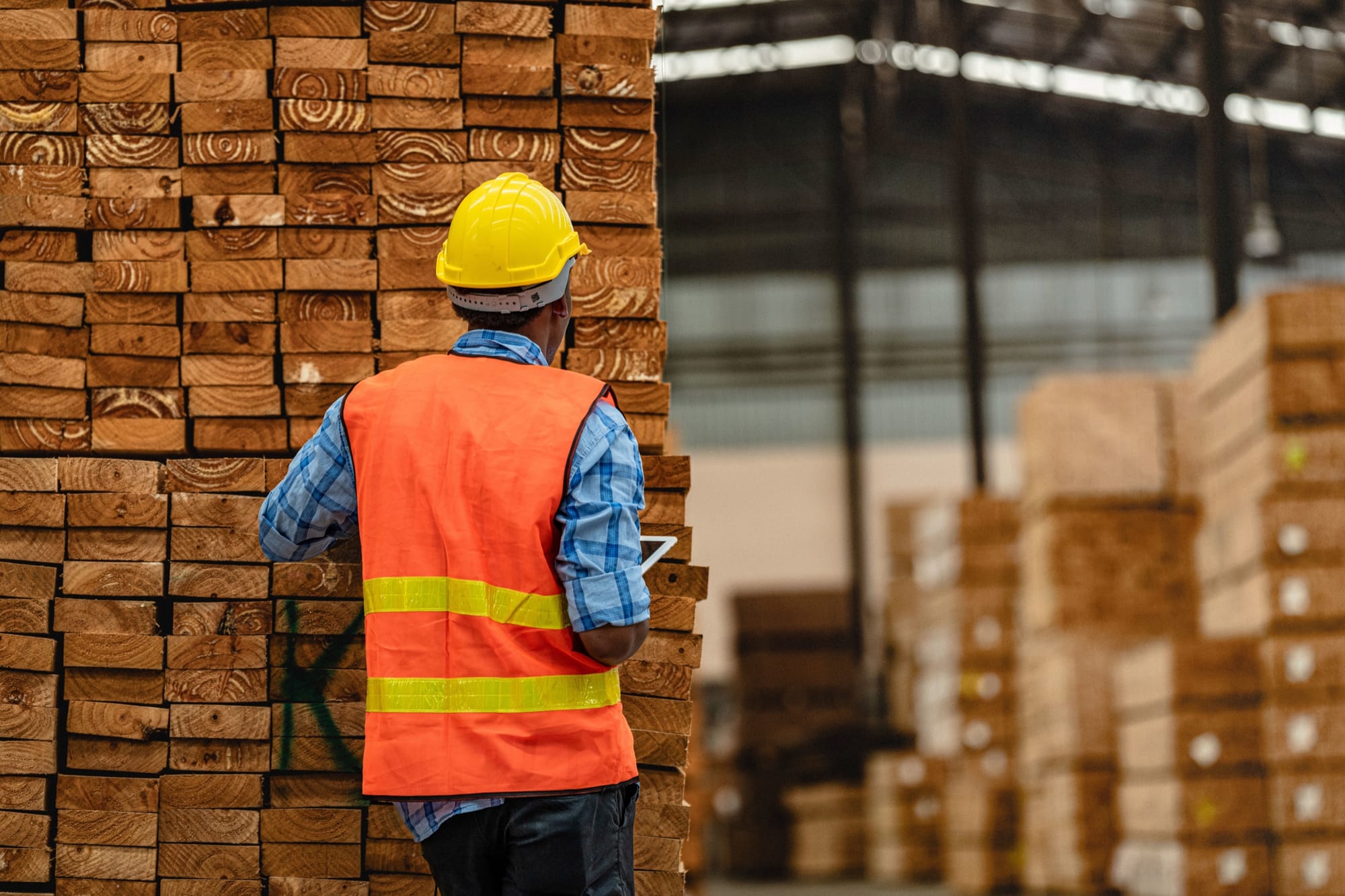 A worker in a high-visibility vest checking stacked lumber