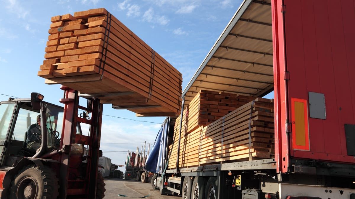 A forklift lifting banded lumber onto a delivery trailer