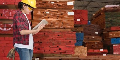 A buyer checking stacked lumber inventory in a warehouse