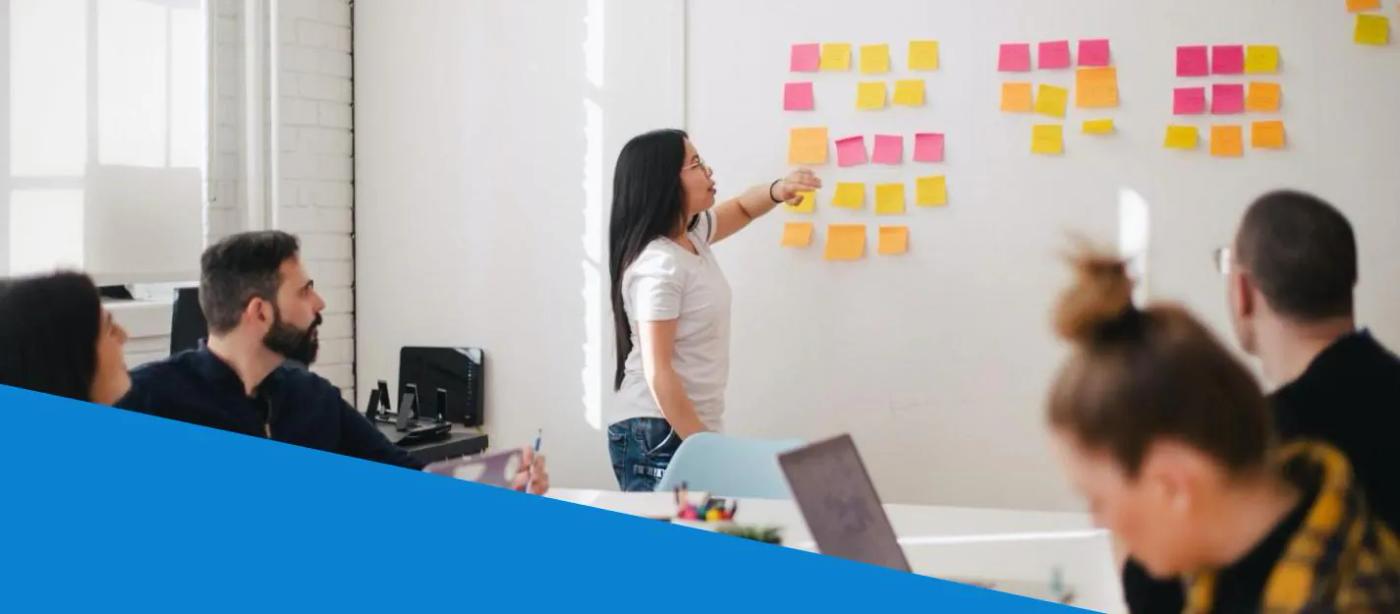 Colleagues discuss a wall of colored notes in a meeting room.