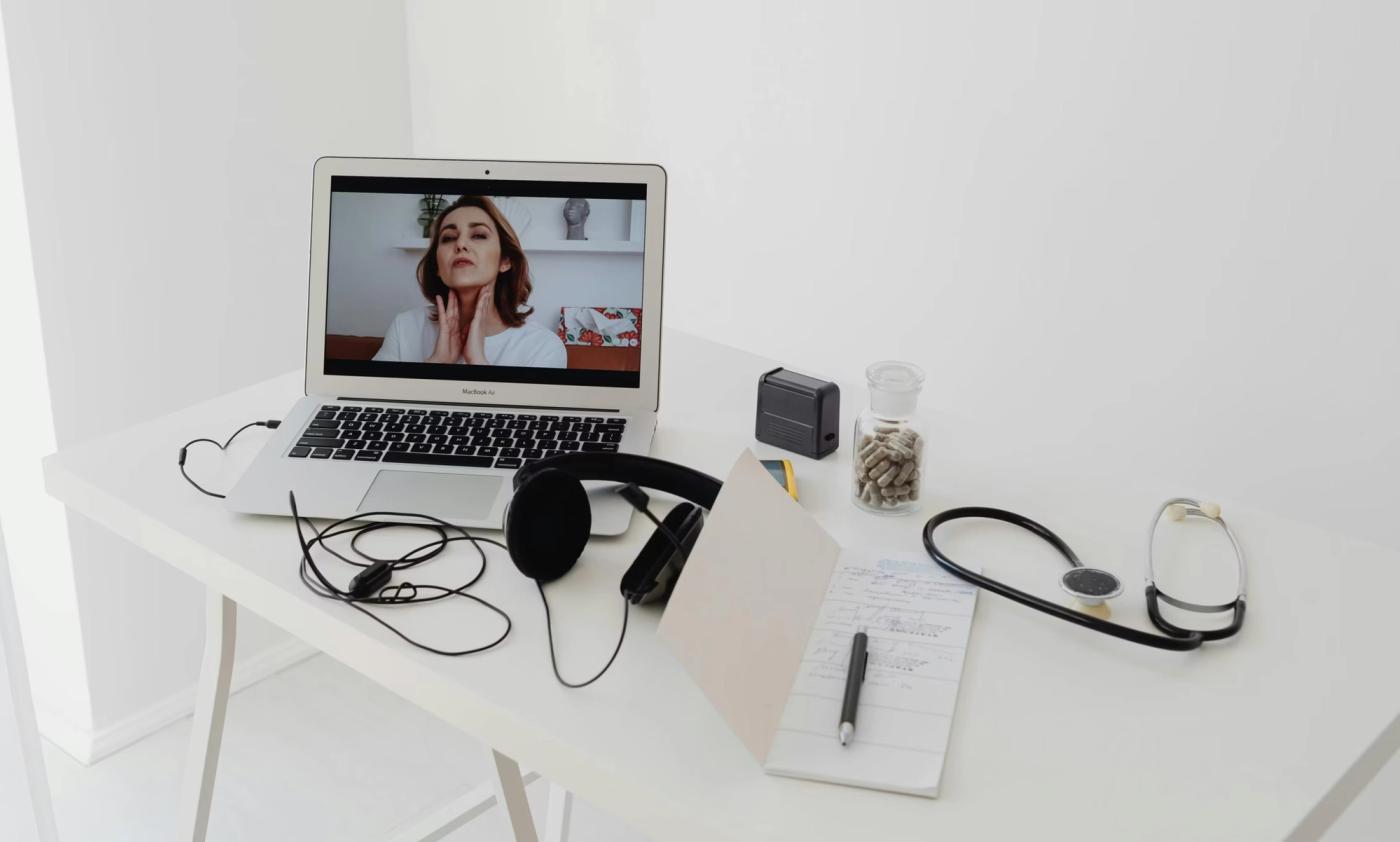 A laptop shows a video consultation beside a stethoscope and an open notebook.