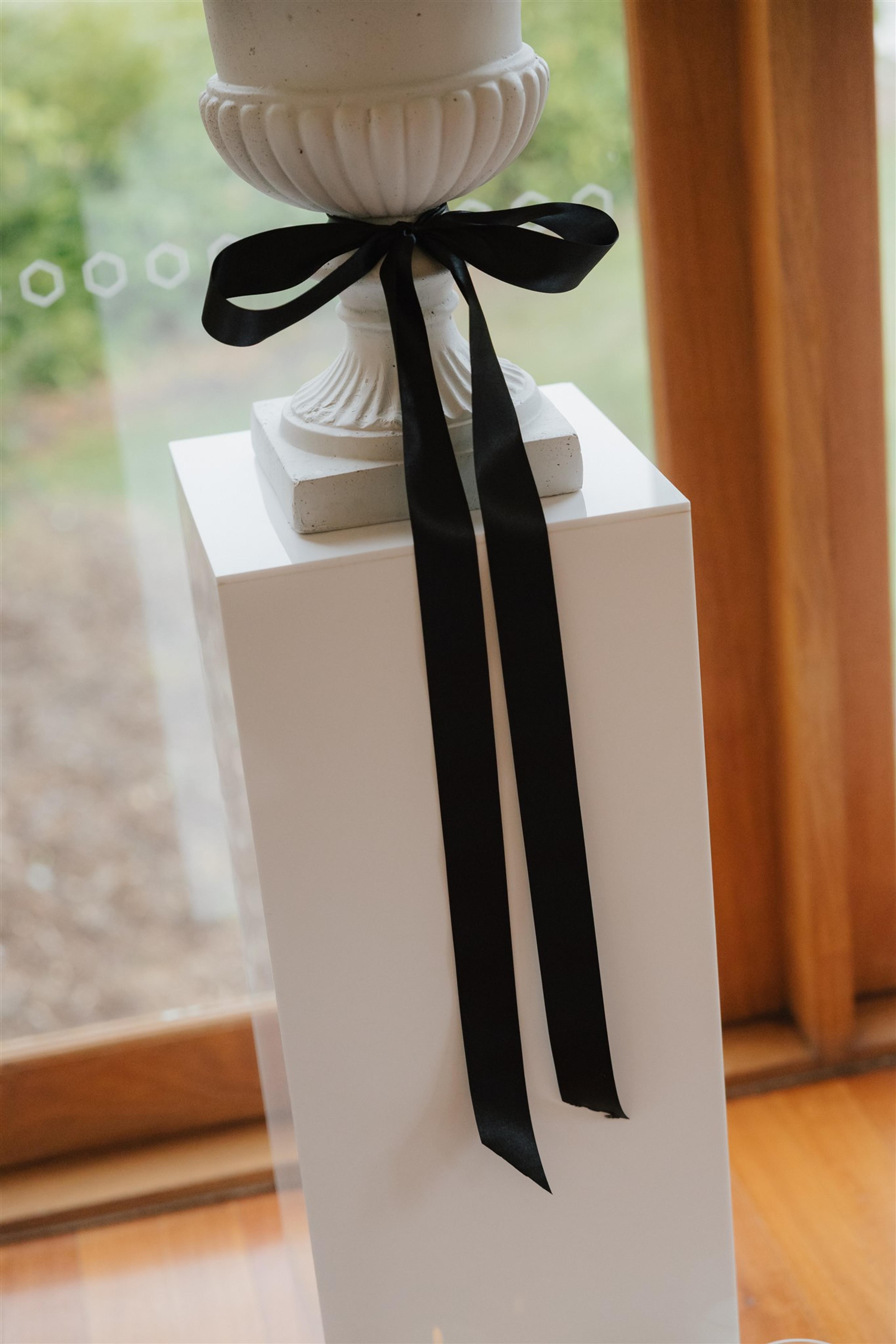 Close-up of a white urn on a plinth finished with black ribbon styling at The Valley Estate Gold Coast wedding.