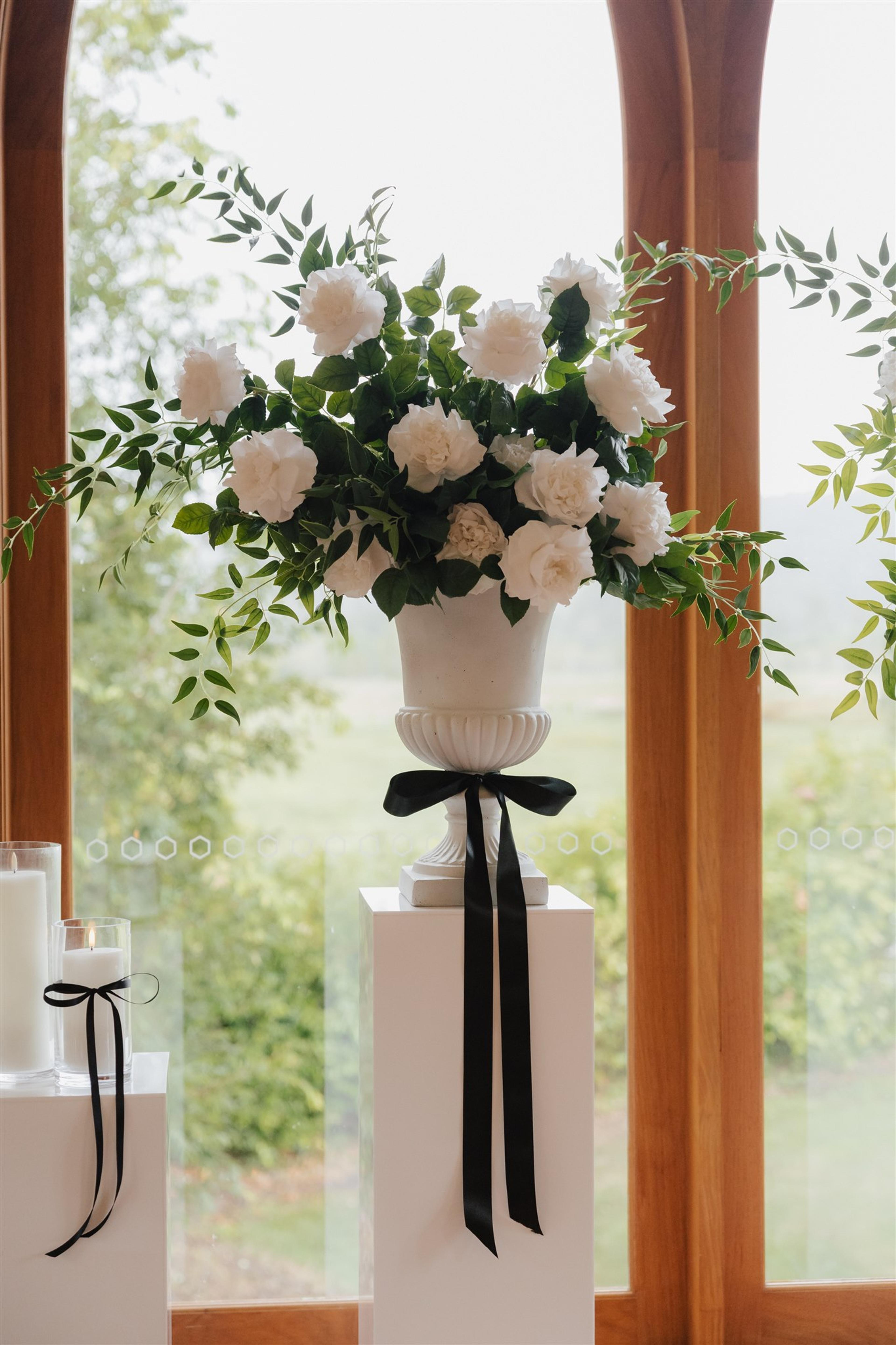White floral ceremony urn with black ribbon detail styled in front of the arched windows at The Valley Estate Gold Coast.
