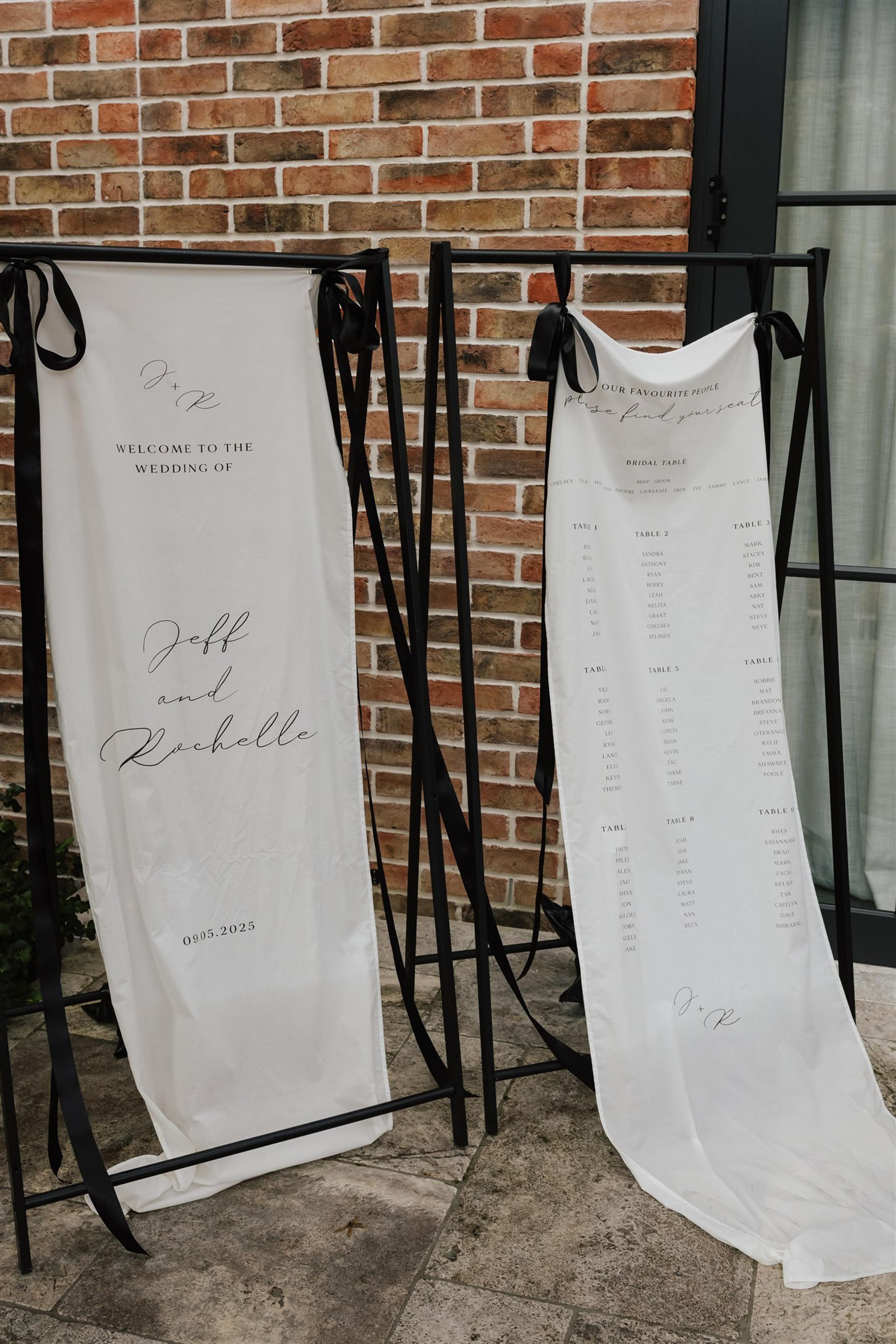Wedding welcome sign and seating chart styled with black ribbons against the brick exterior of The Valley Estate Gold Coast.