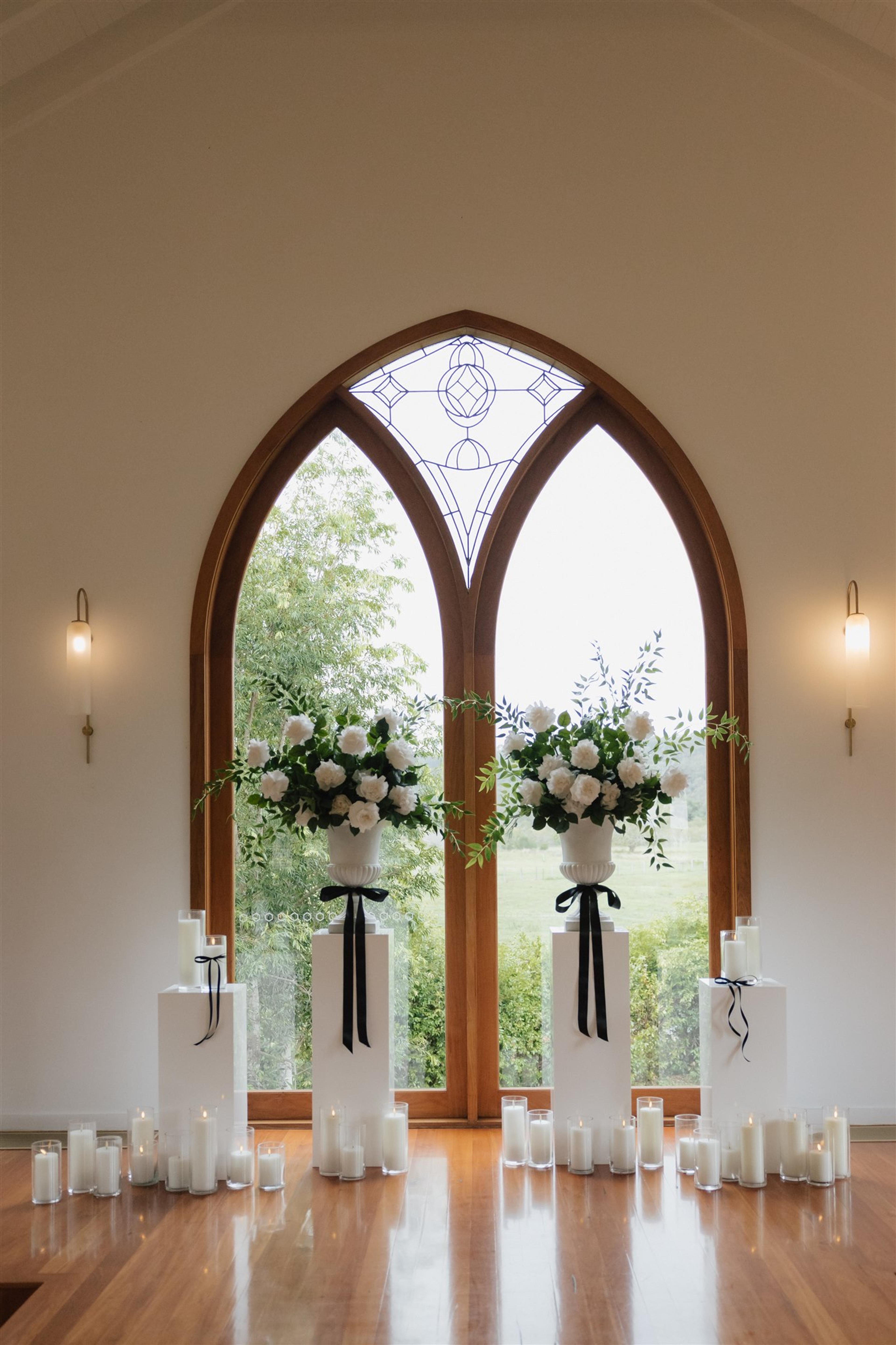 Ceremony styling at The Valley Estate Gold Coast with white floral urns, black ribbon details and candlelit plinths for Rochelle and Jeff’s wedding.