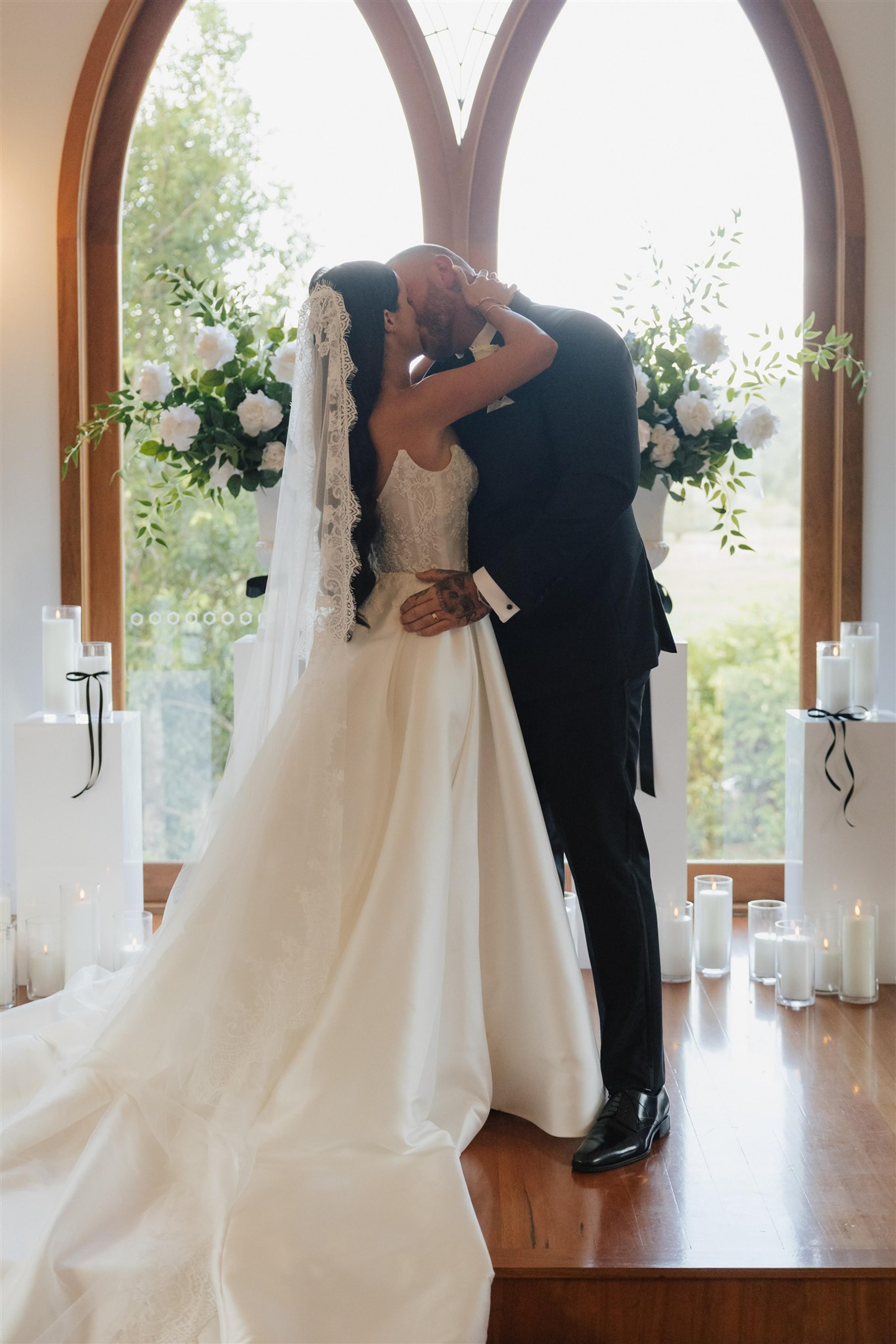 Rochelle and Jeff sharing their first kiss in front of white floral ceremony styling and candlelight at The Valley Estate Gold Coast.