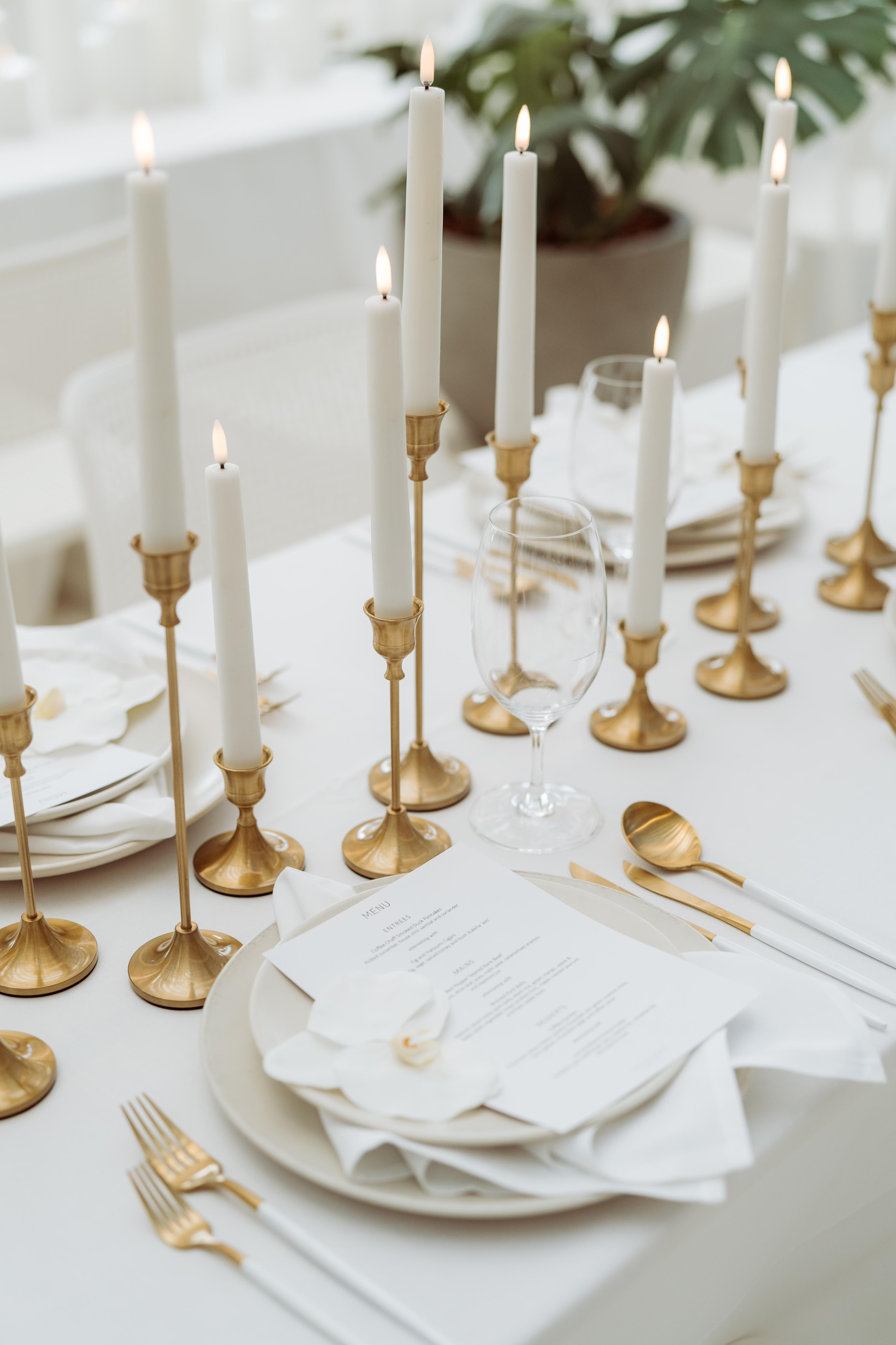 Close-up of white taper candles in gold candle holders on a refined Industry Beans Newstead event tablescape.