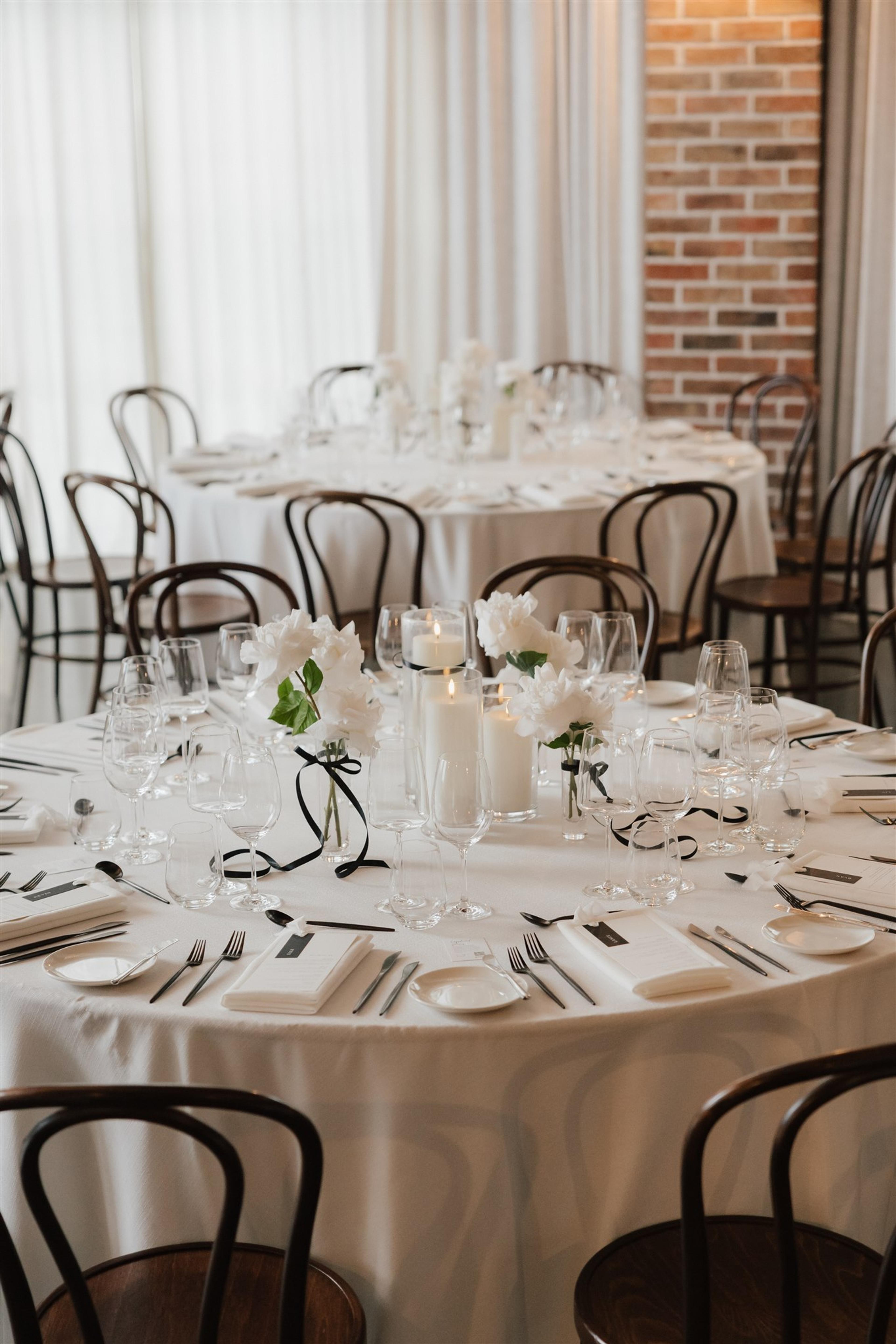Round wedding reception tables styled with white roses, candlelight and black ribbon details at The Valley Estate Gold Coast.