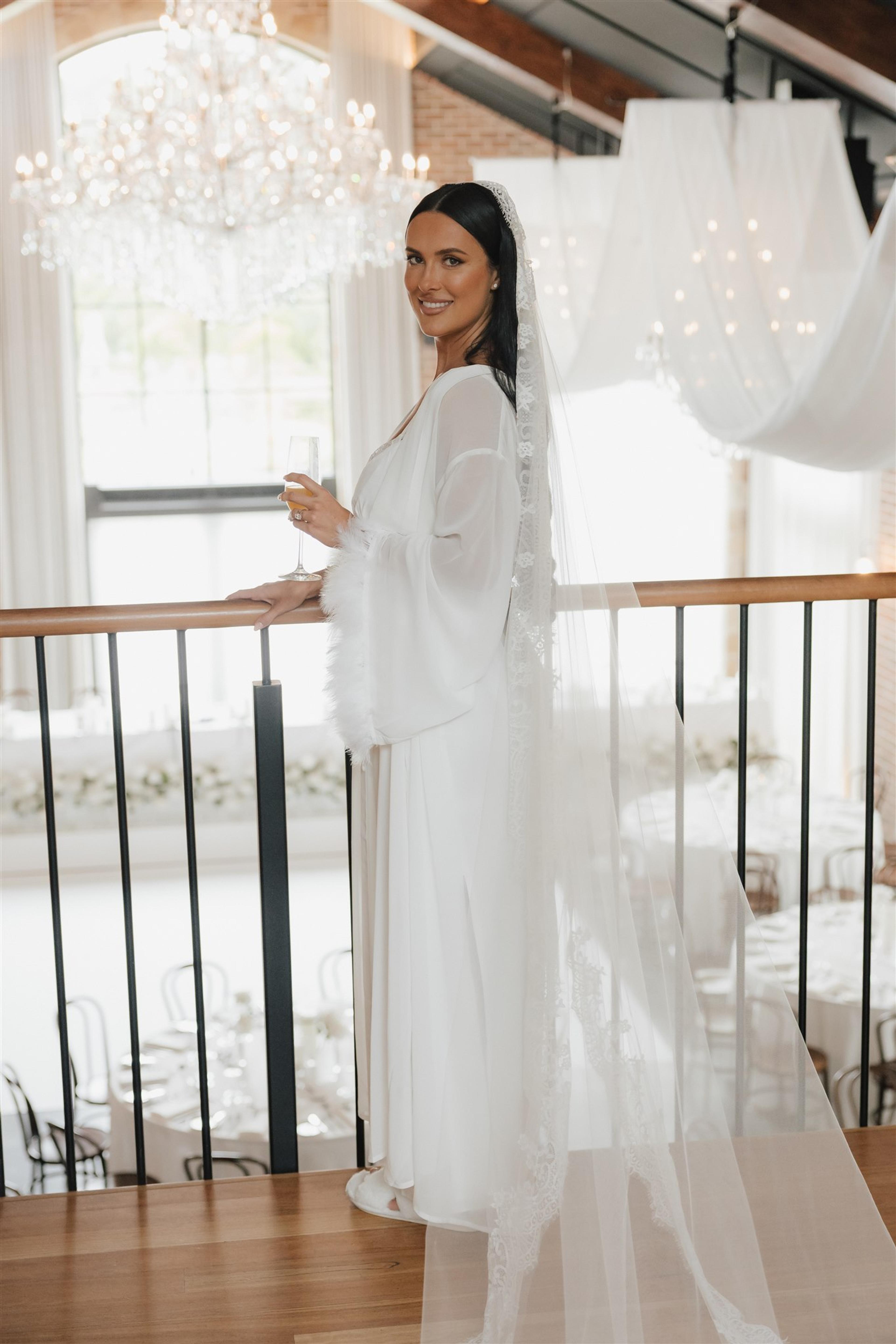 Bride Rochelle in a white robe and lace veil overlooking The Valley Estate wedding reception space on the Gold Coast.