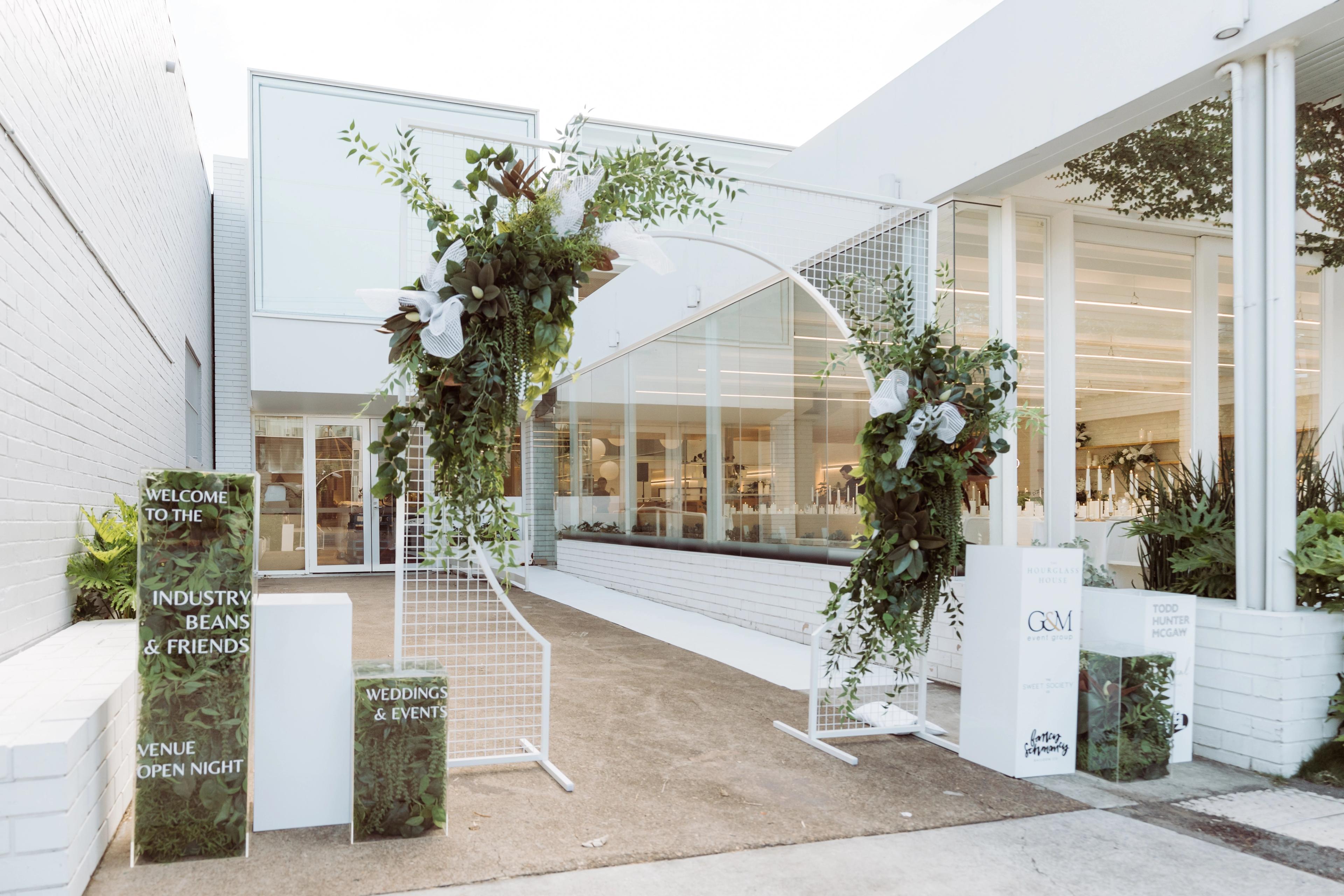 Entrance styling for the Industry Beans Newstead brand activation in Brisbane, featuring a white arch with lush greenery and event signage.
