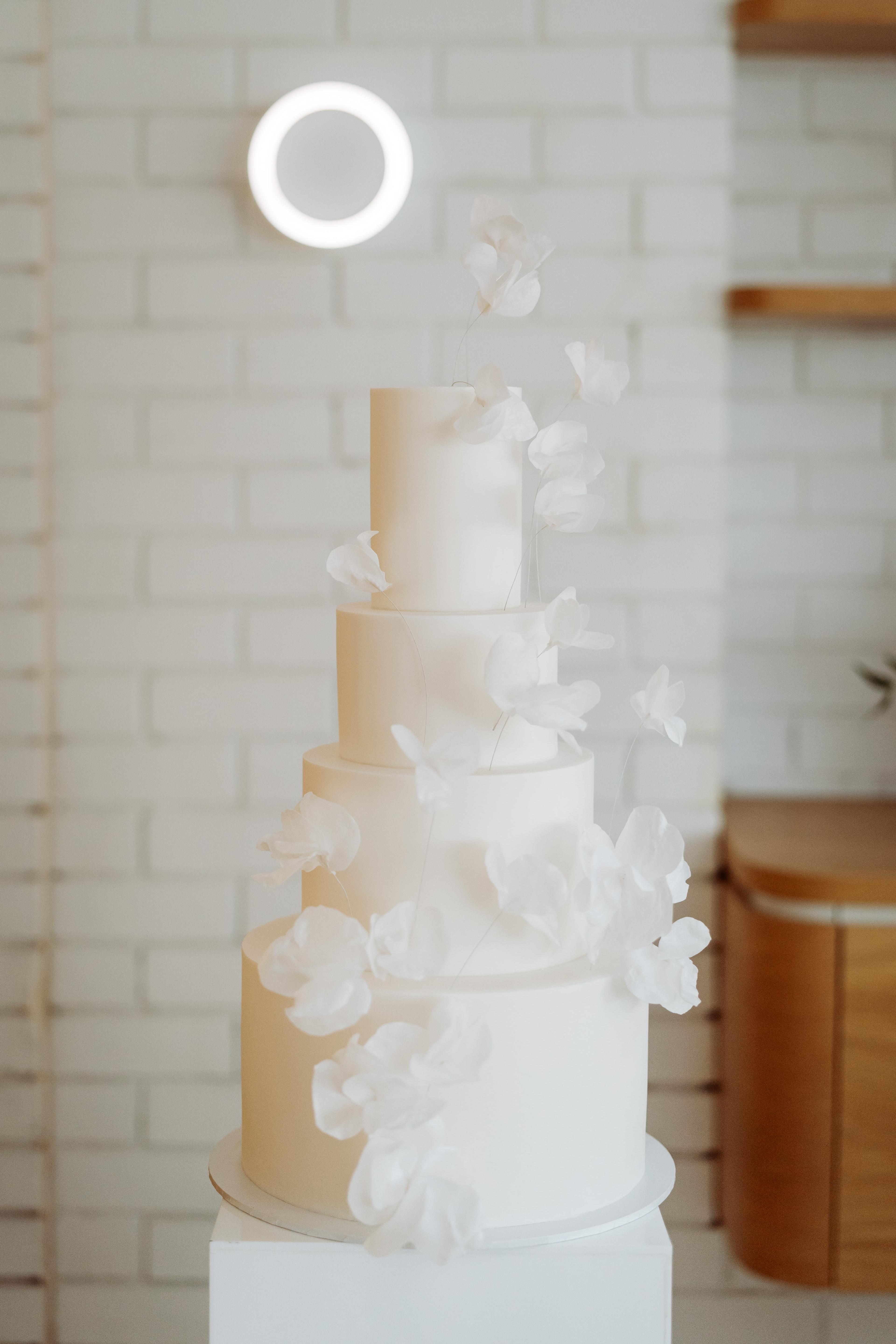 Minimal white tiered cake with soft floral detailing displayed at the Industry Beans Newstead brand activation in Brisbane.