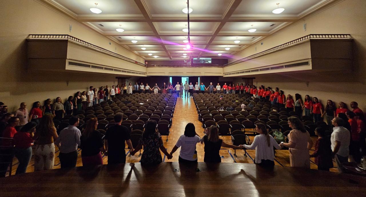 Educadores formam uma roda de mãos dadas durante atividade de acolhimento no teatro
