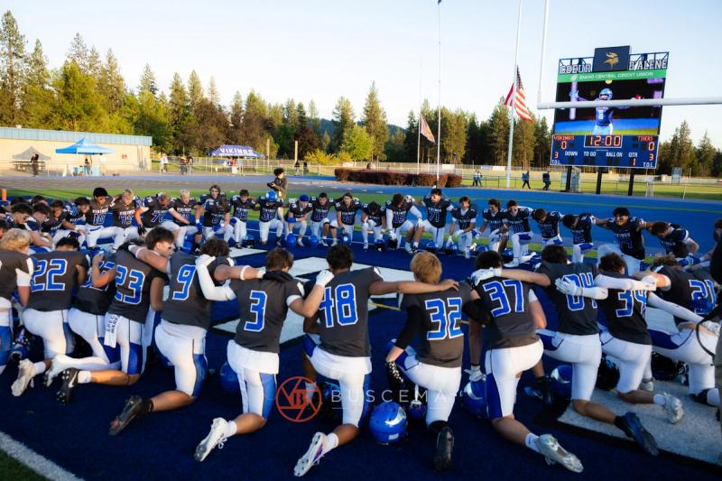 Coeur d'Alene Vikings football team kneeling together on the field before kickoff