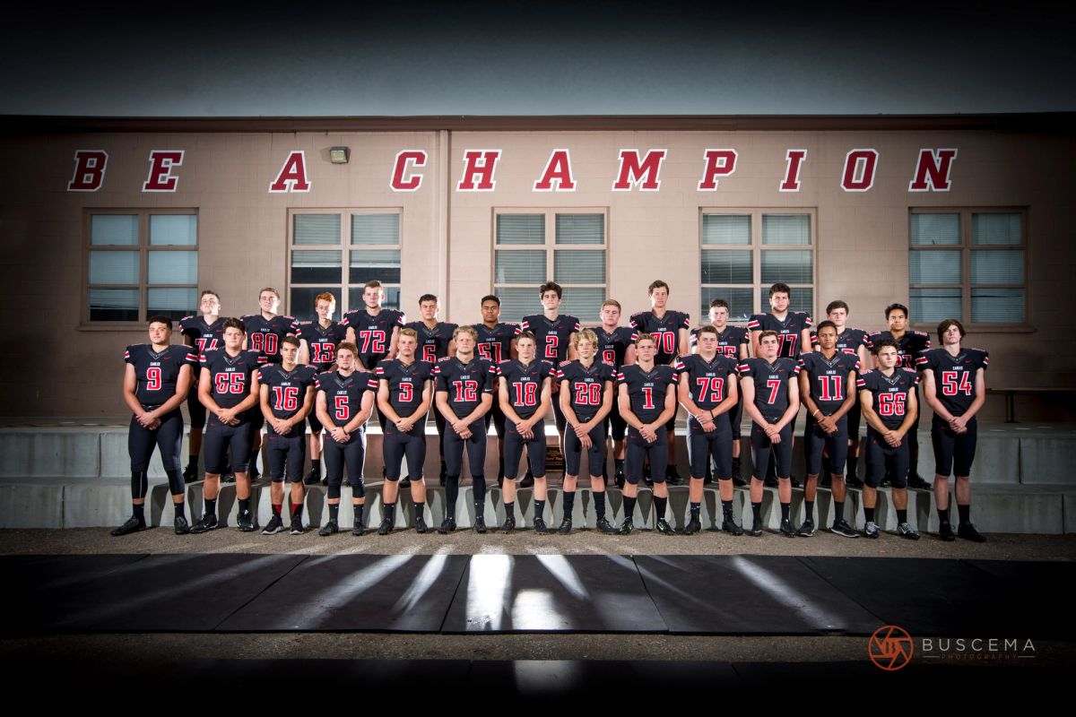 Coeur d'Alene High School varsity football team posed in front of "Be A Champion" building signage.